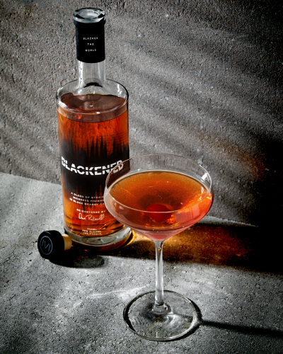 Manhattan Cocktail in a Coupe Glass in front of a bottle of BLACKENED American Whiskey