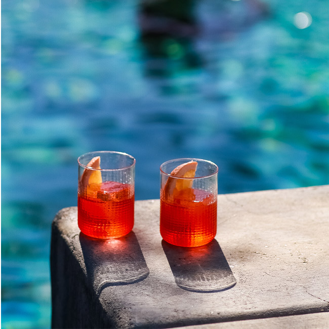 Two summer whiskey cocktails in glasses next to a pool