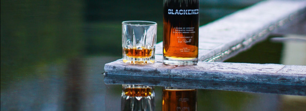 A Bottle of BLACKENED and a Whiskey Glass by the Water